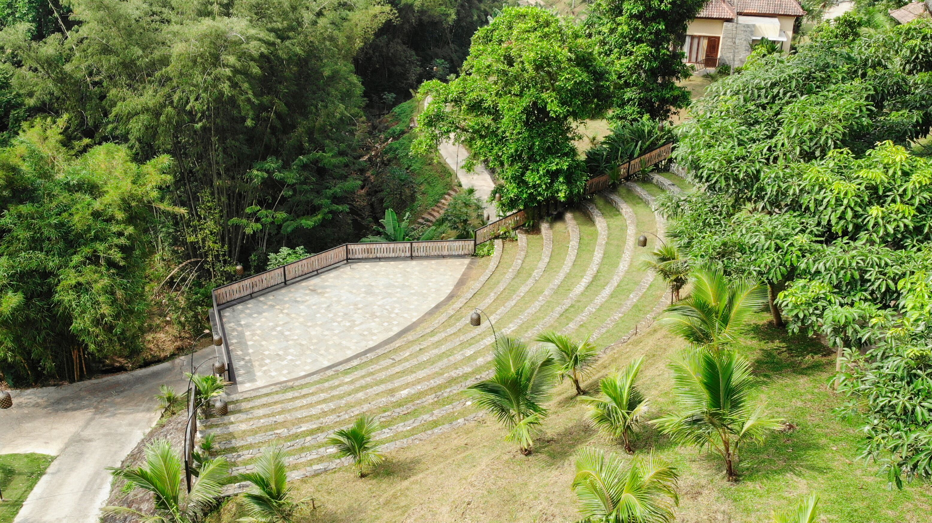 A terraced garden with stone steps and palm trees, surrounded by dense greenery and a building in the background.
