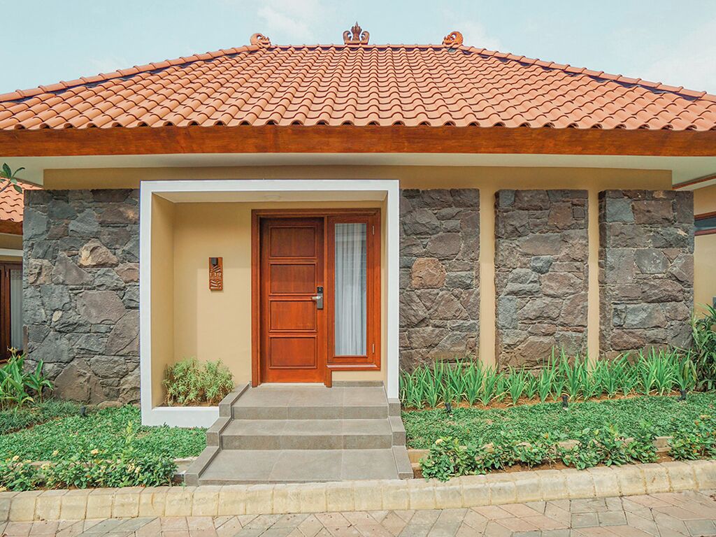 Uma casa com telhado de telhas, paredes de pedra, porta de madeira e um pequeno jardim frontal.