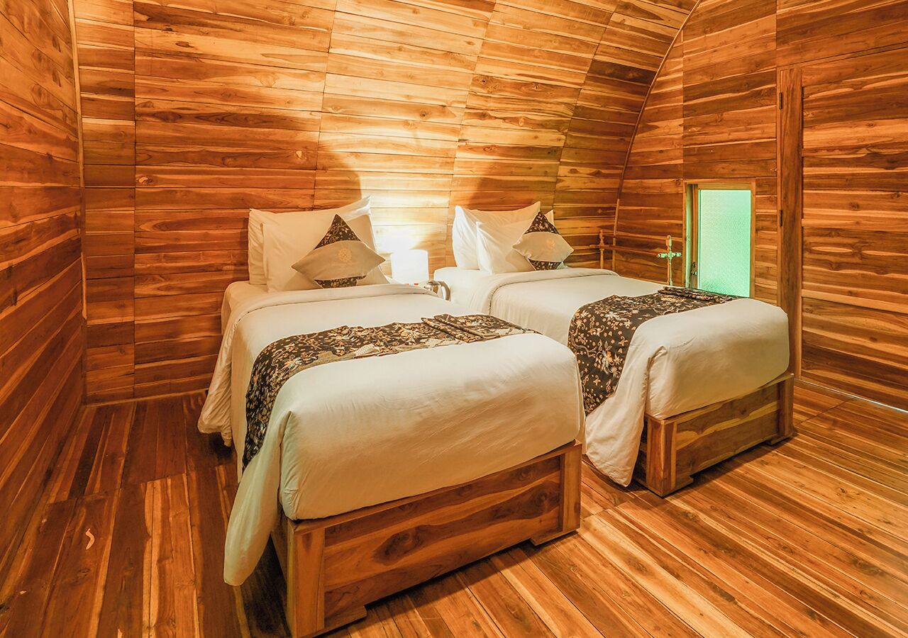 A wooden cabin room with two beds, a green door, and a small table.