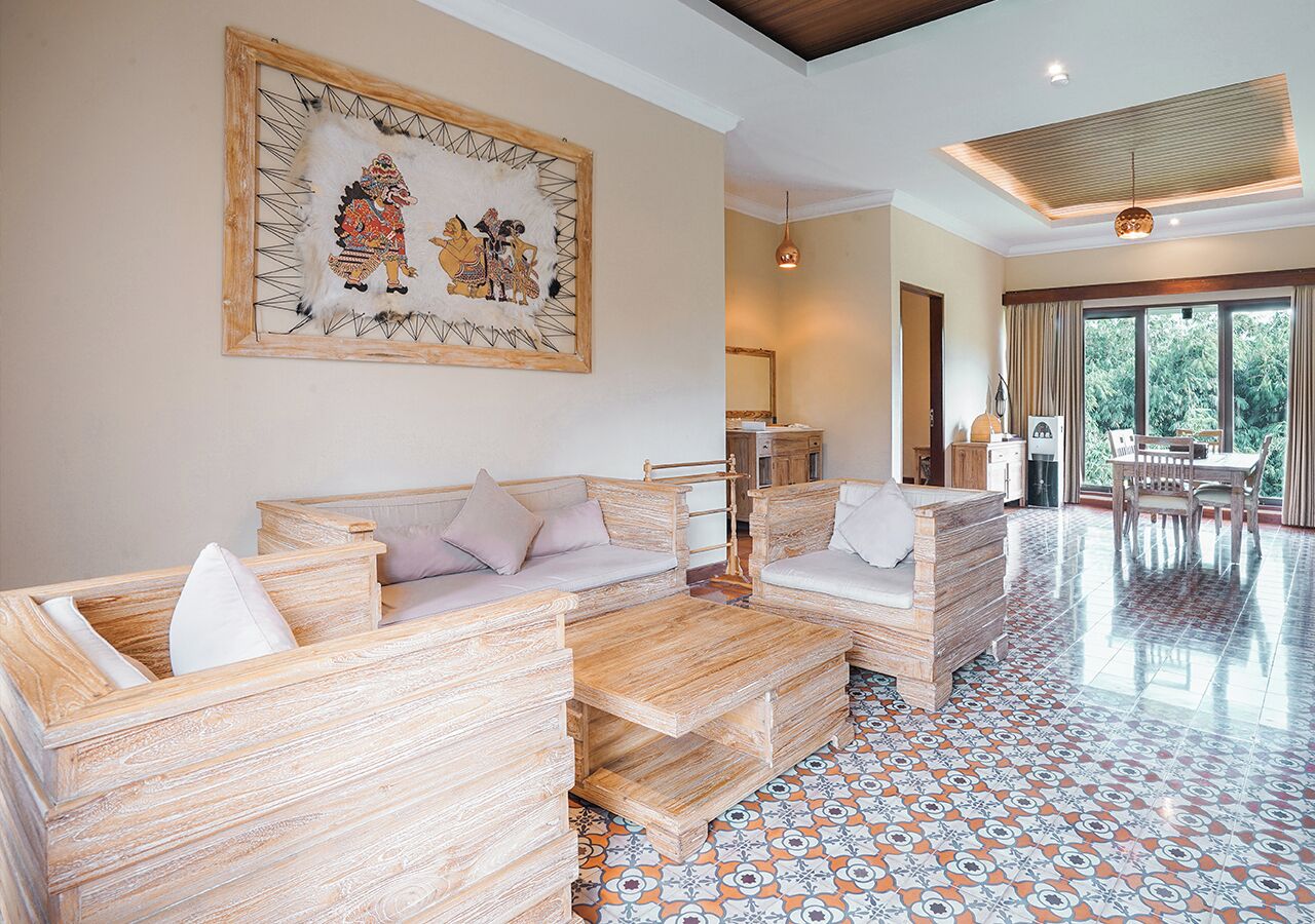 A spacious living area with a sofa set and a dining table, a large framed artwork on the wall, and a patterned floor.