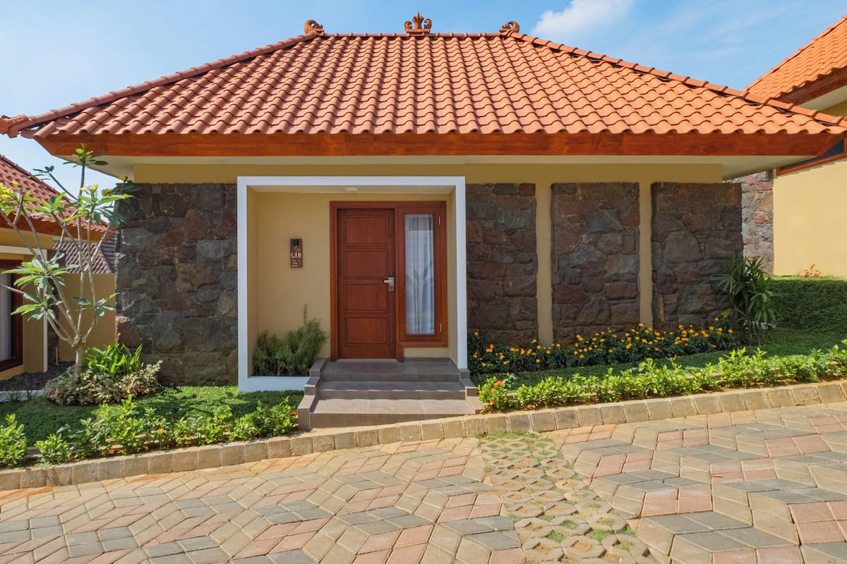 Una casa con techo de tejas, paredes de piedra, puerta de madera y entrada pavimentada.