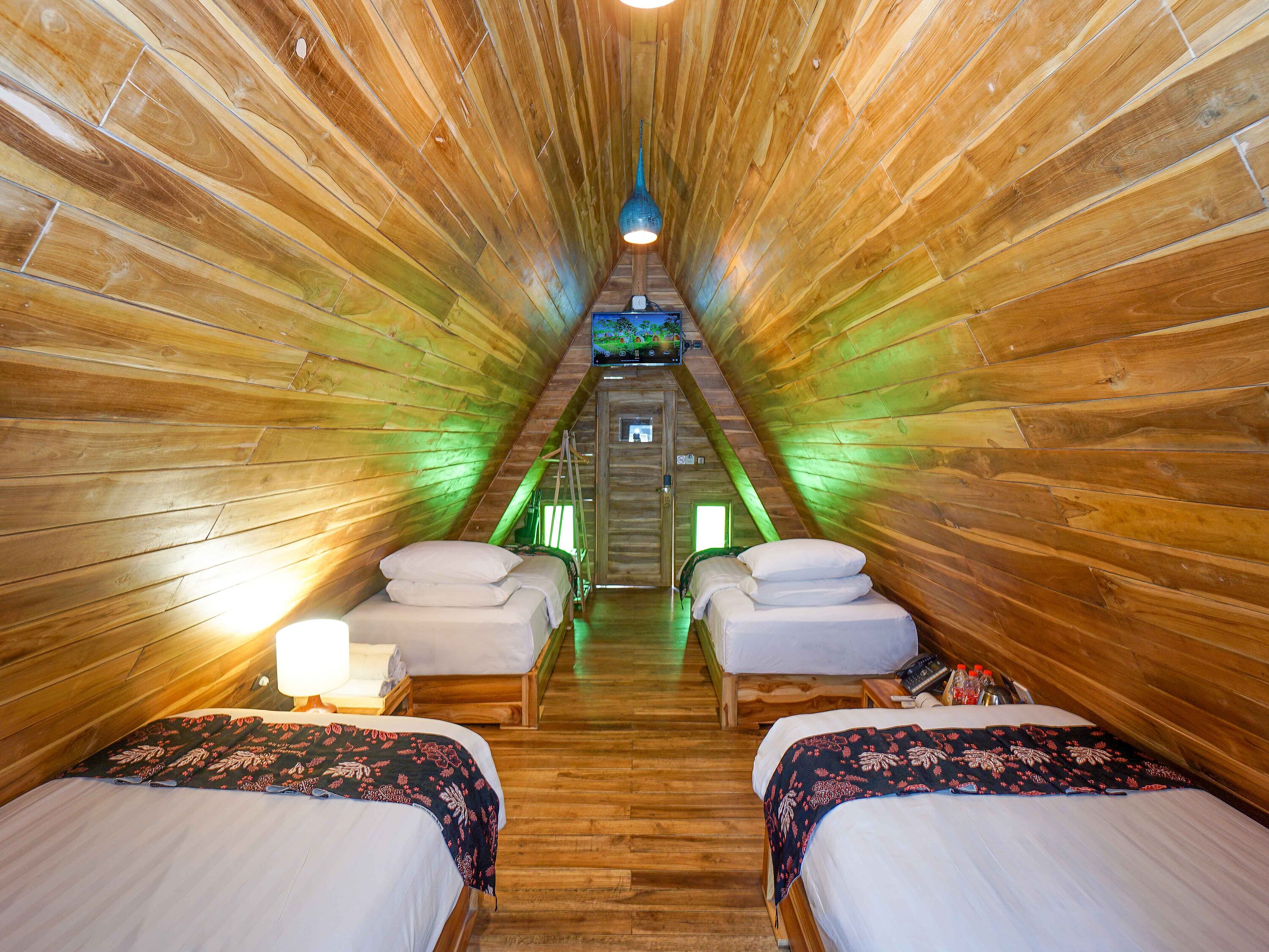 A wooden interior with two beds, a small table, and a hanging light fixture.