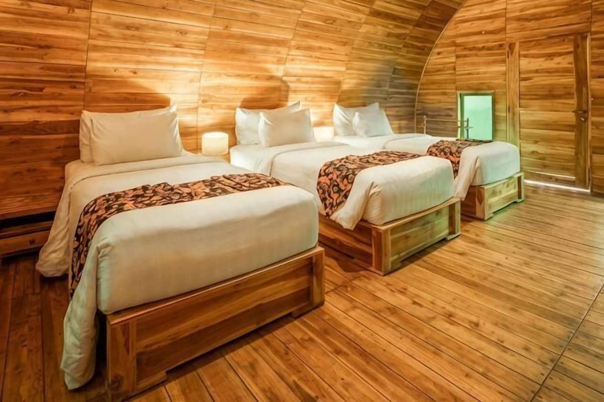 Habitación tipo cabaña de madera con tres camas, cada una con ropa blanca y un edredón estampado.