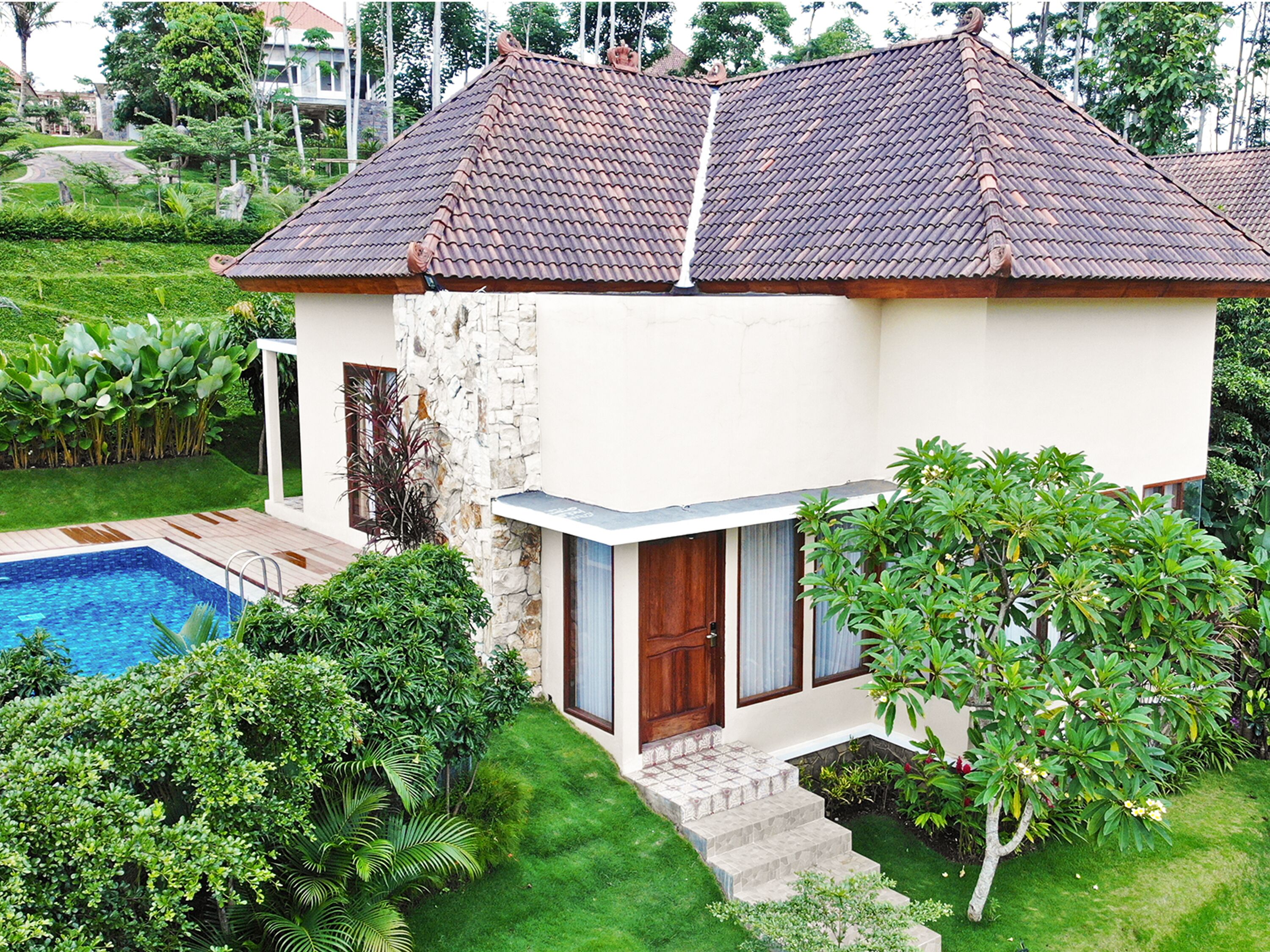 A two-story house with a swimming pool, surrounded by lush greenery and a well-maintained lawn.