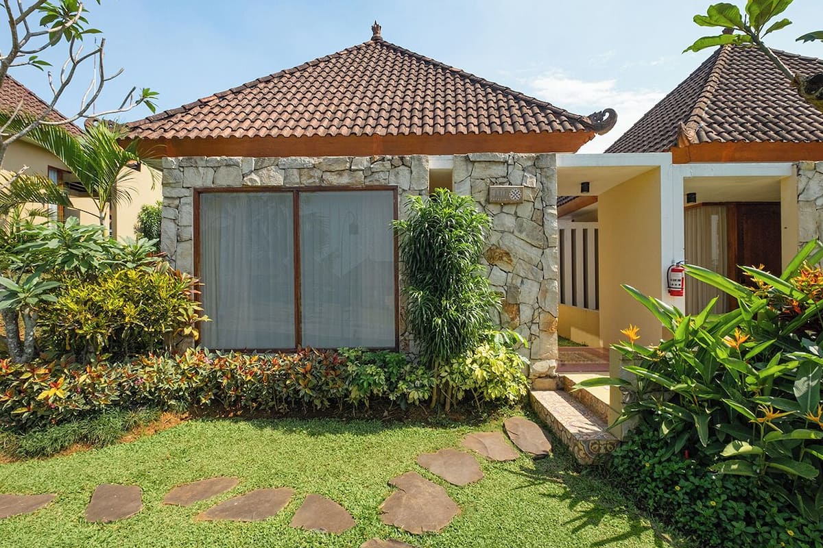Una casa con fachada de piedra, techo de tejas y un jardín bien cuidado con piedras y diversas plantas.