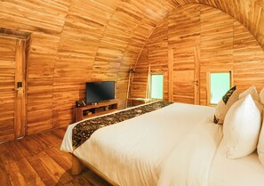 A cozy room with wooden walls, a bed with white bedding, a television on a wooden stand, and a window with a view. - Shanaya Resort Malang (Malang)