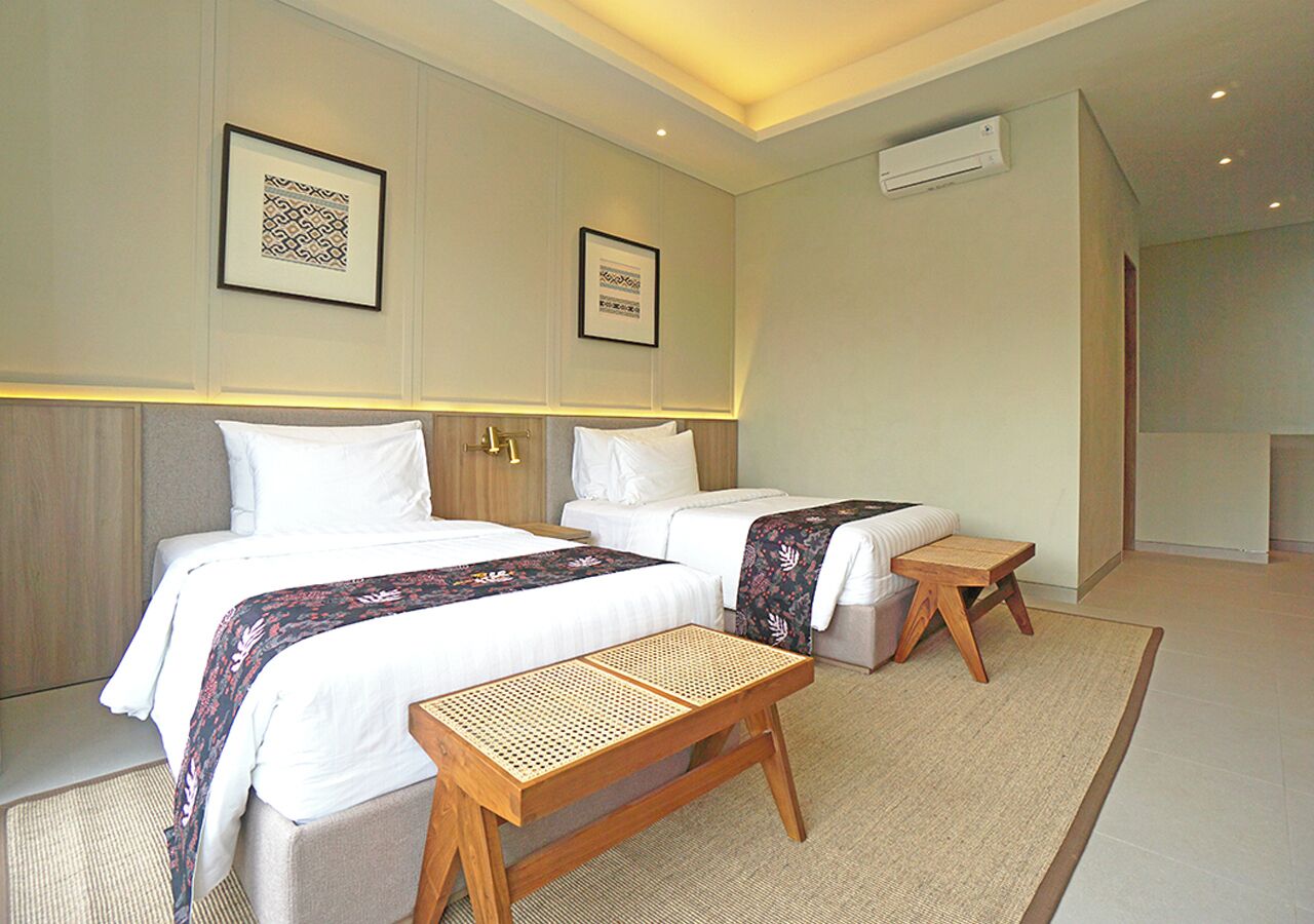 A hotel room with two beds, a small table, and a bench.