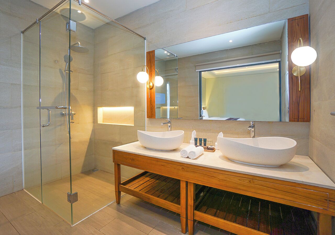 Une salle de bain moderne dotée d’une douche à parois de verre, de deux vasques et d’un grand miroir au-dessus du meuble-lavabo.