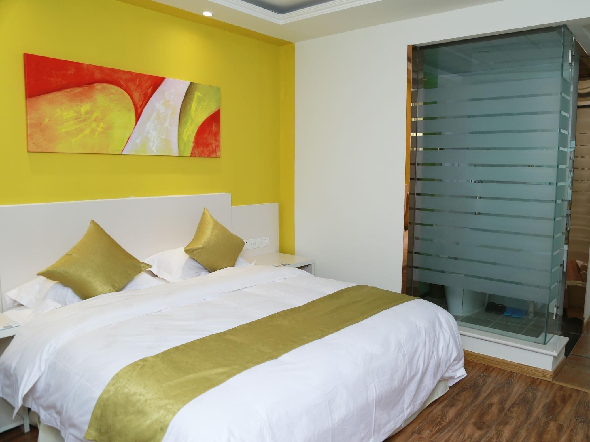 Une chambre d’hôtel avec un lit, une armoire à portes vitrées et un mur jaune orné d’un tableau.
