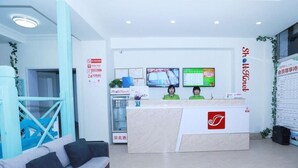 Zona de recepció d'hotel amb taulell de recepció, dos monitors, un sofà i una escala.