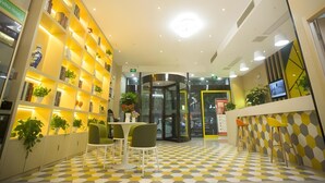 Un interior moderno con suelo a cuadros, una zona de estar central con sillas, una puerta giratoria y un estante iluminado en amarillo con plantas.