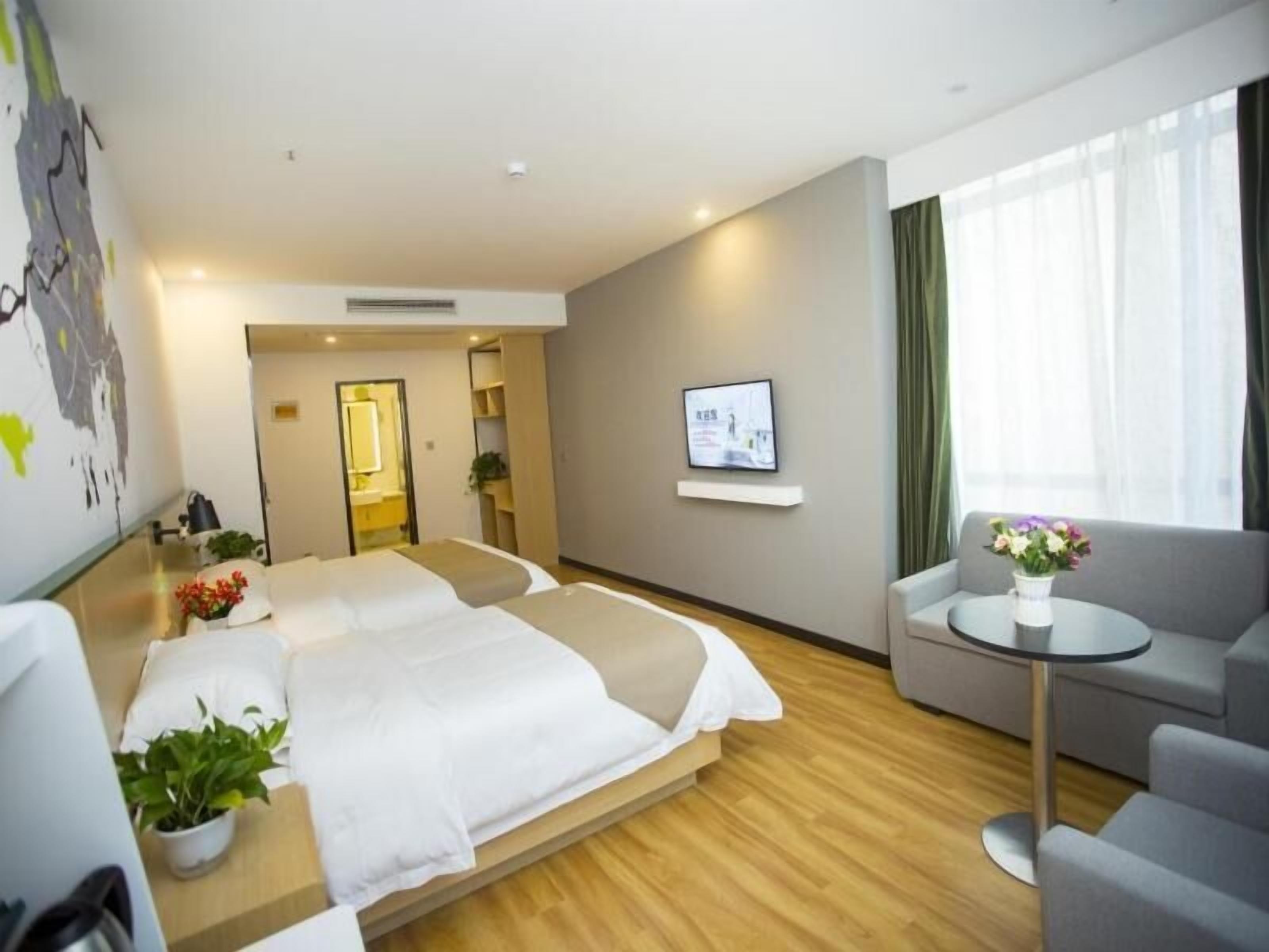 A hotel room with two beds, a TV, a small table with a vase, and a sofa.