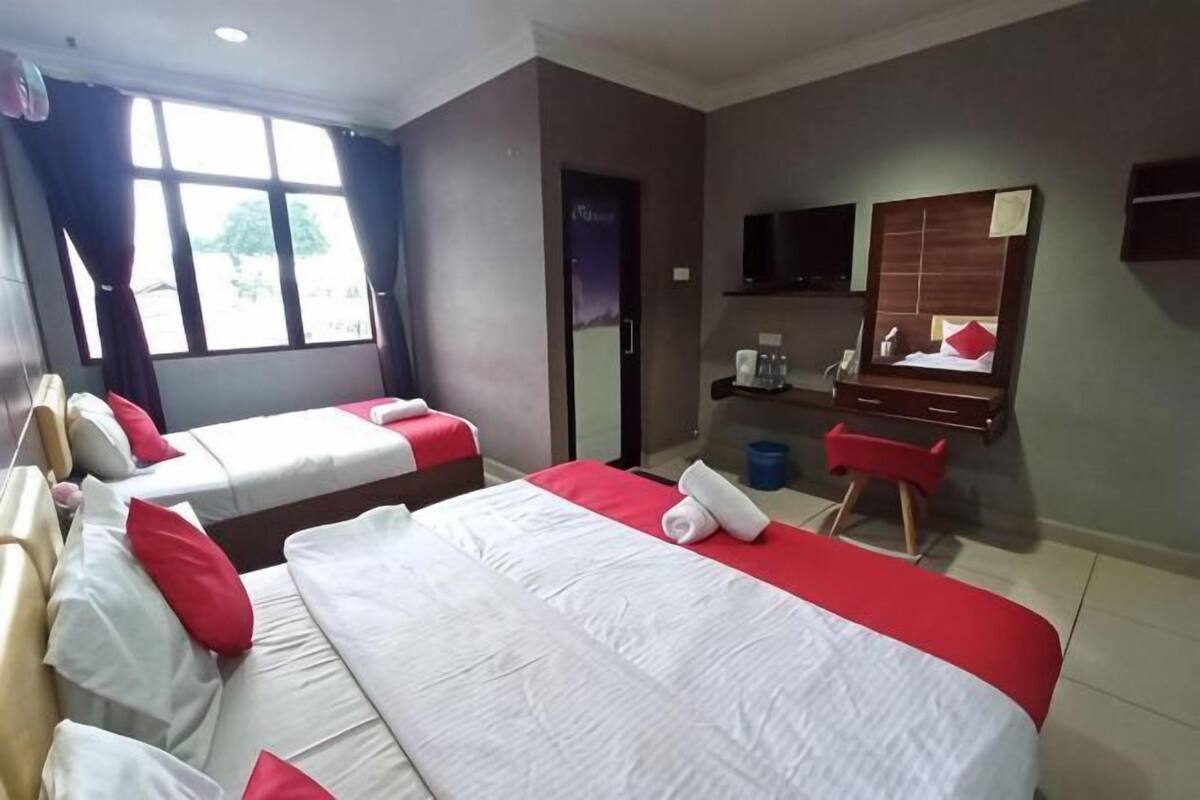 Una camera d'albergo con due letti, una scrivania, una sedia, una televisione e una finestra con tende.