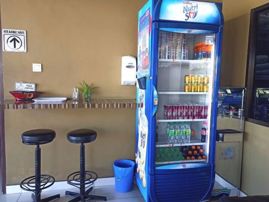 Máquina de vendas com diversas bebidas e lanches, balcão com bancos e um aviso indicando uma escada.