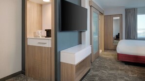 Une chambre d’hôtel équipée d’un téléviseur à écran plat fixé au mur, d’une armoire en bois, d’une table de chevet et d’un lit avec une tête de lit rouge.