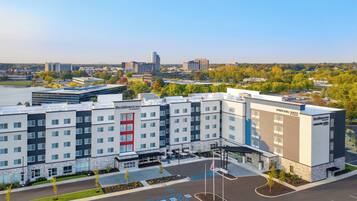 Ett hotell med flera våningar och modern design, med en parkeringsplats där det finns markerade platser för rörelsehindrade, och utsikt över den omgivande stadsbilden.