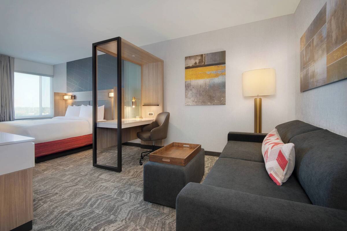 A hotel room with a bed, a desk, a chair, a sofa, and a small table.