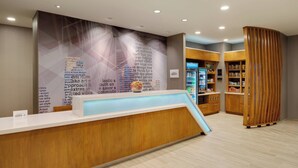 Un espace d'accueil au design moderne, comprenant un comptoir d'accueil en bois, un mur orné de textes et de motifs graphiques, et un présentoir pour les boissons.