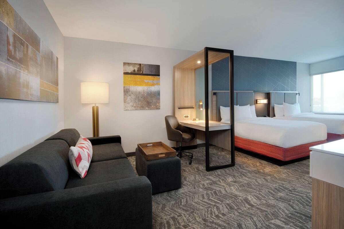 A hotel room with a bed, a desk, a chair, a sofa, and a large window.
