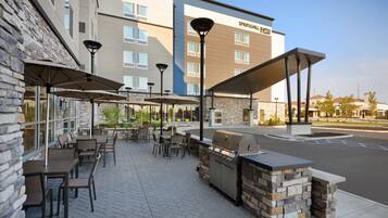 An outdoor patio area with tables and chairs, a barbecue grill, and umbrellas.
