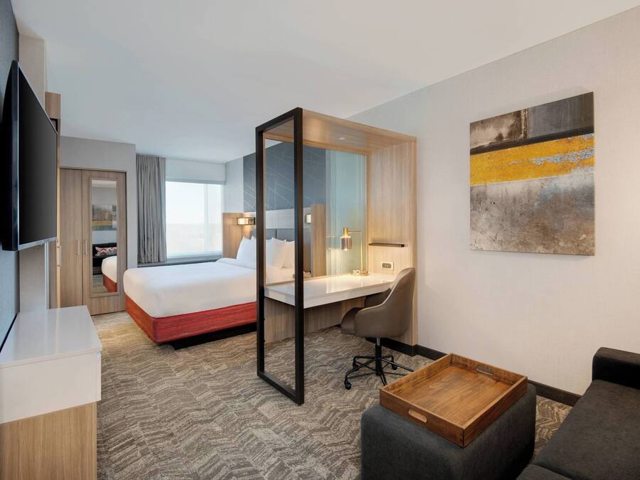 A hotel room with a bed, a desk, a chair, a TV, and a painting on the wall.