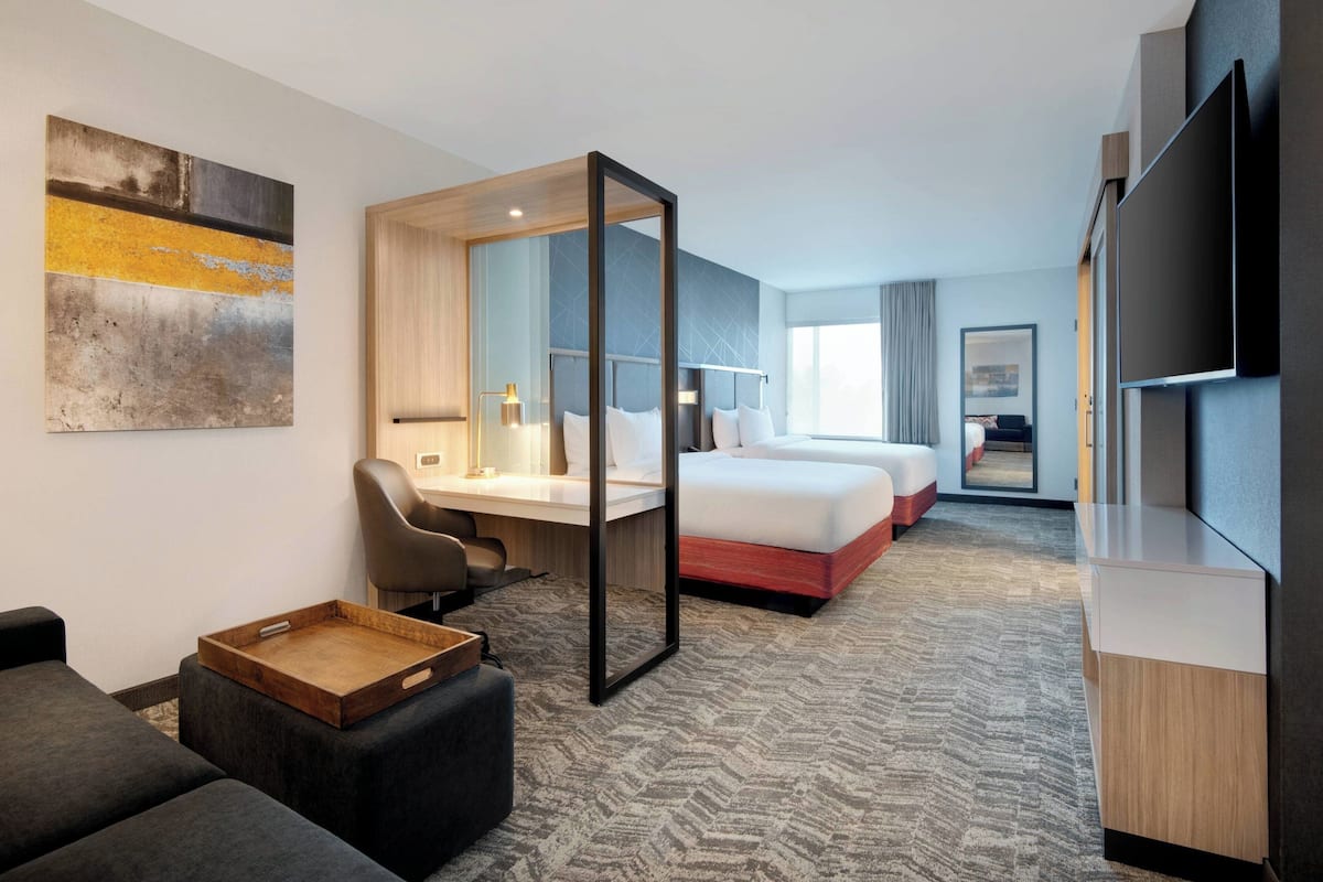 A hotel room with a bed, a desk, a chair, a TV, and a painting on the wall.