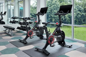A gym with stationary bikes, dumbbells, and a bench.