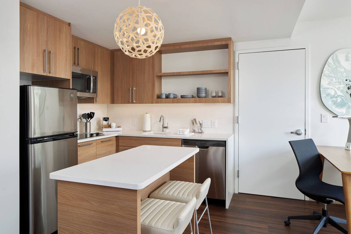 Una cucina moderna con mobili in legno, elettrodomestici in acciaio inox, un piano di lavoro bianco e un'area pranzo con una sedia nera.