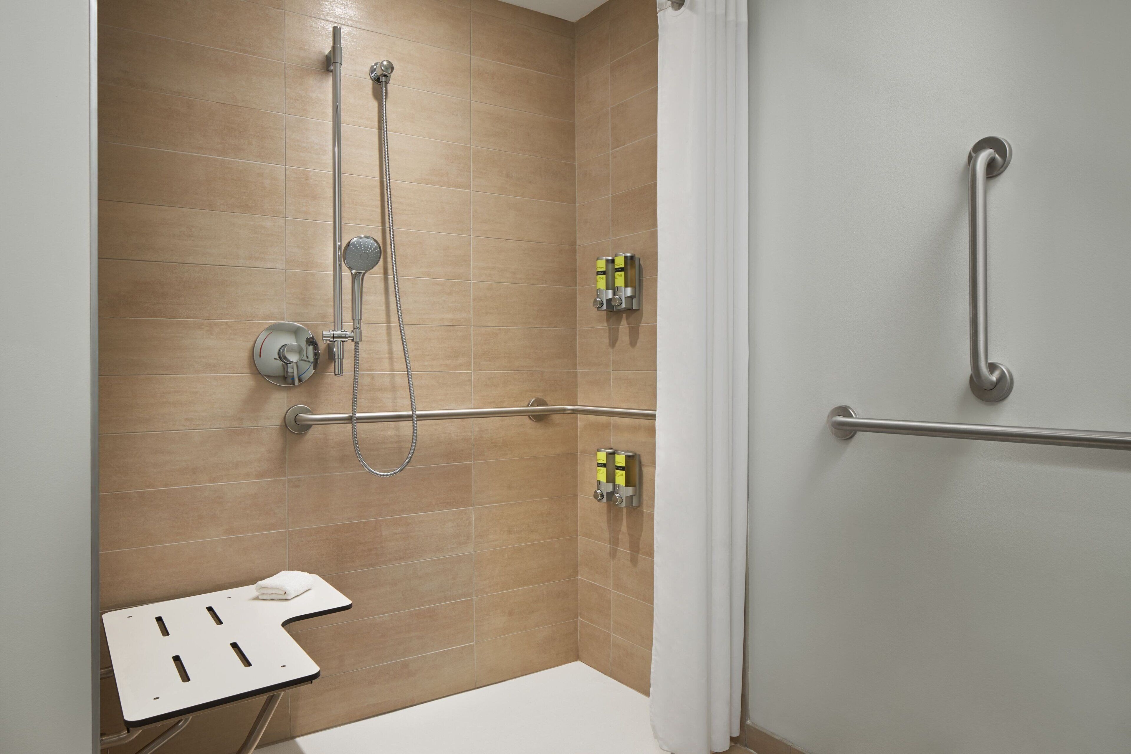 Un baño moderno con ducha, barras de apoyo y una toalla blanca sobre un pequeño banco.