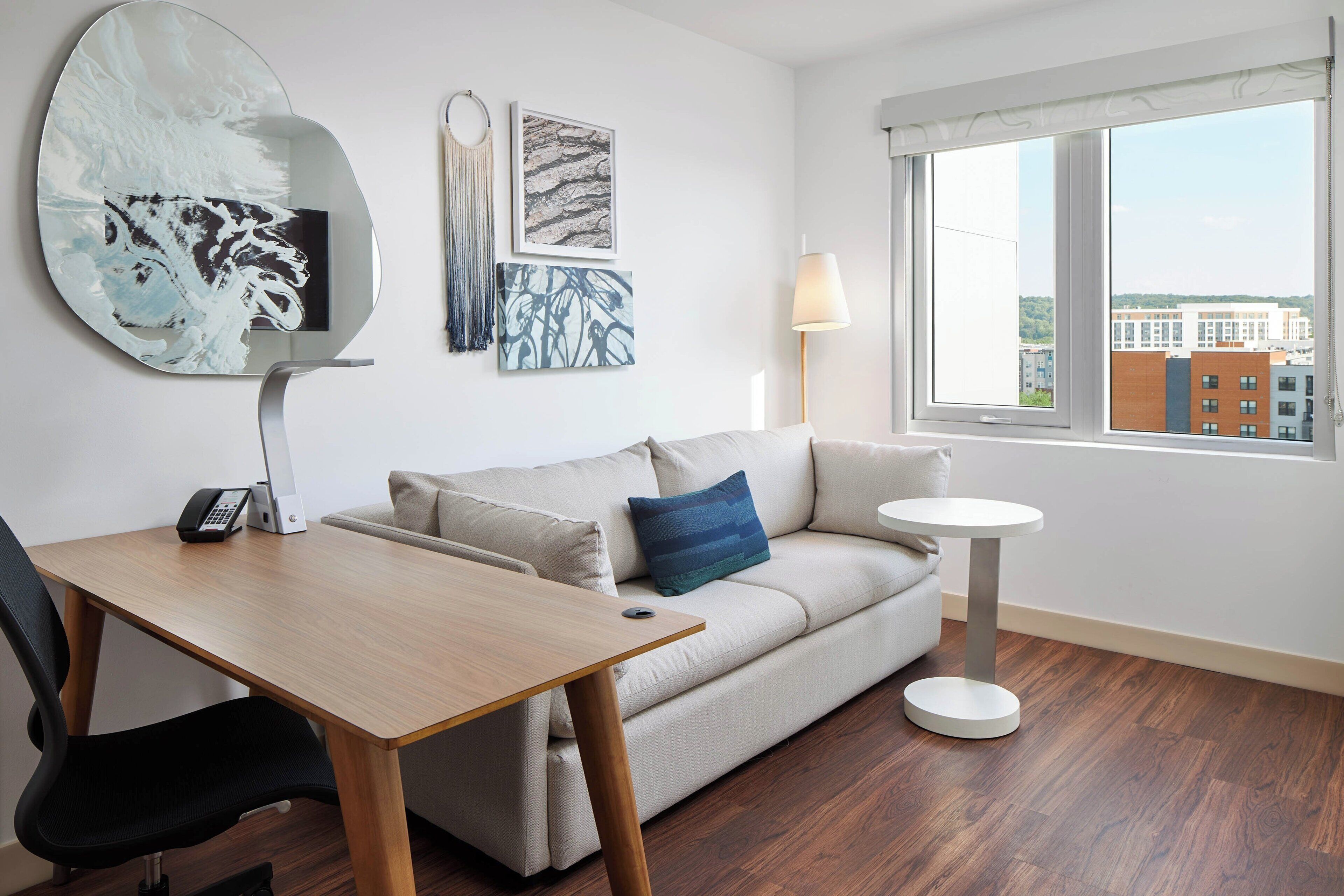 Una habitación moderna con sofá, una mesa redonda, escritorio y un ventanal con vistas a la ciudad.