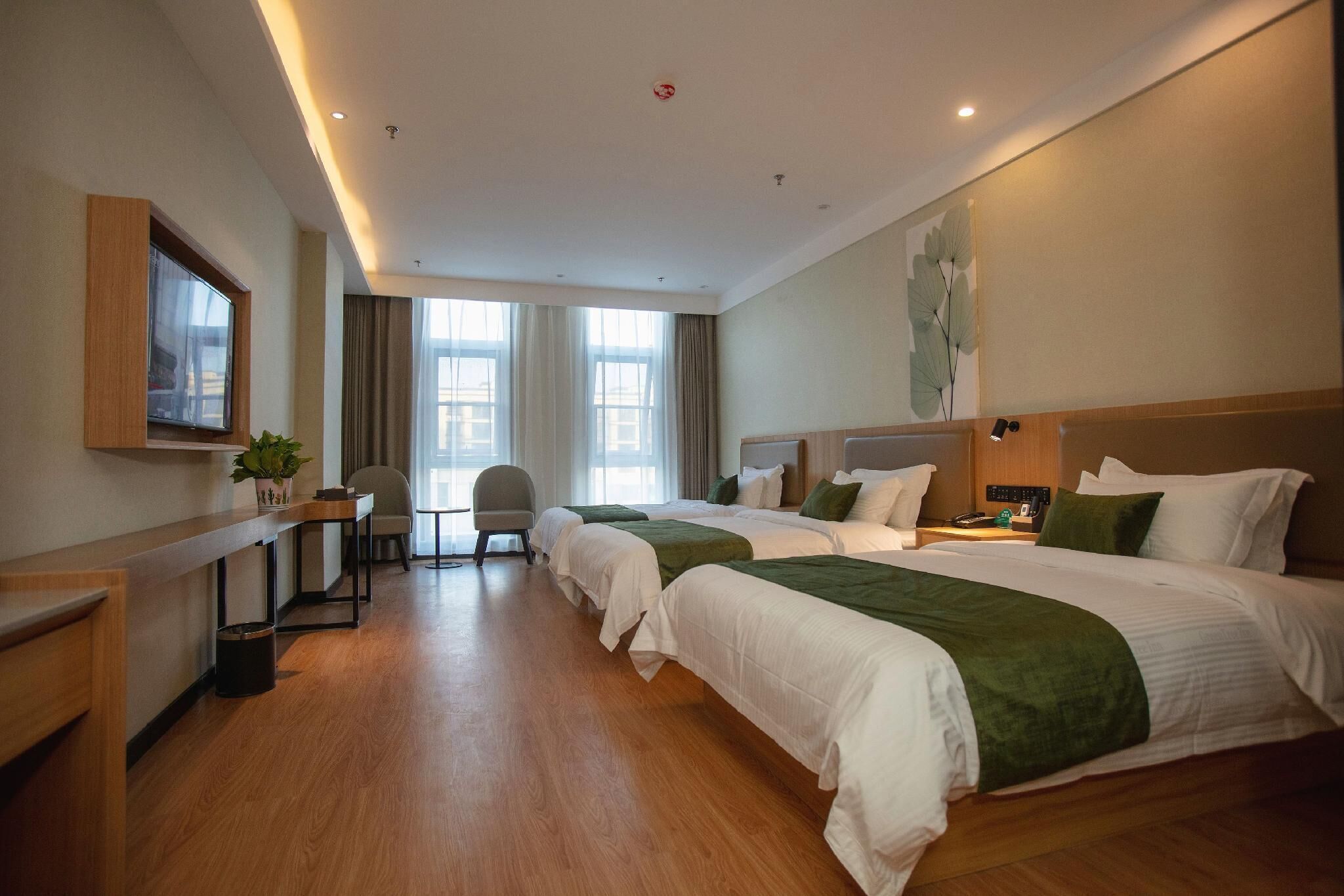 Una habitación de hotel con tres camas, un escritorio, una silla y un ventanal grande.