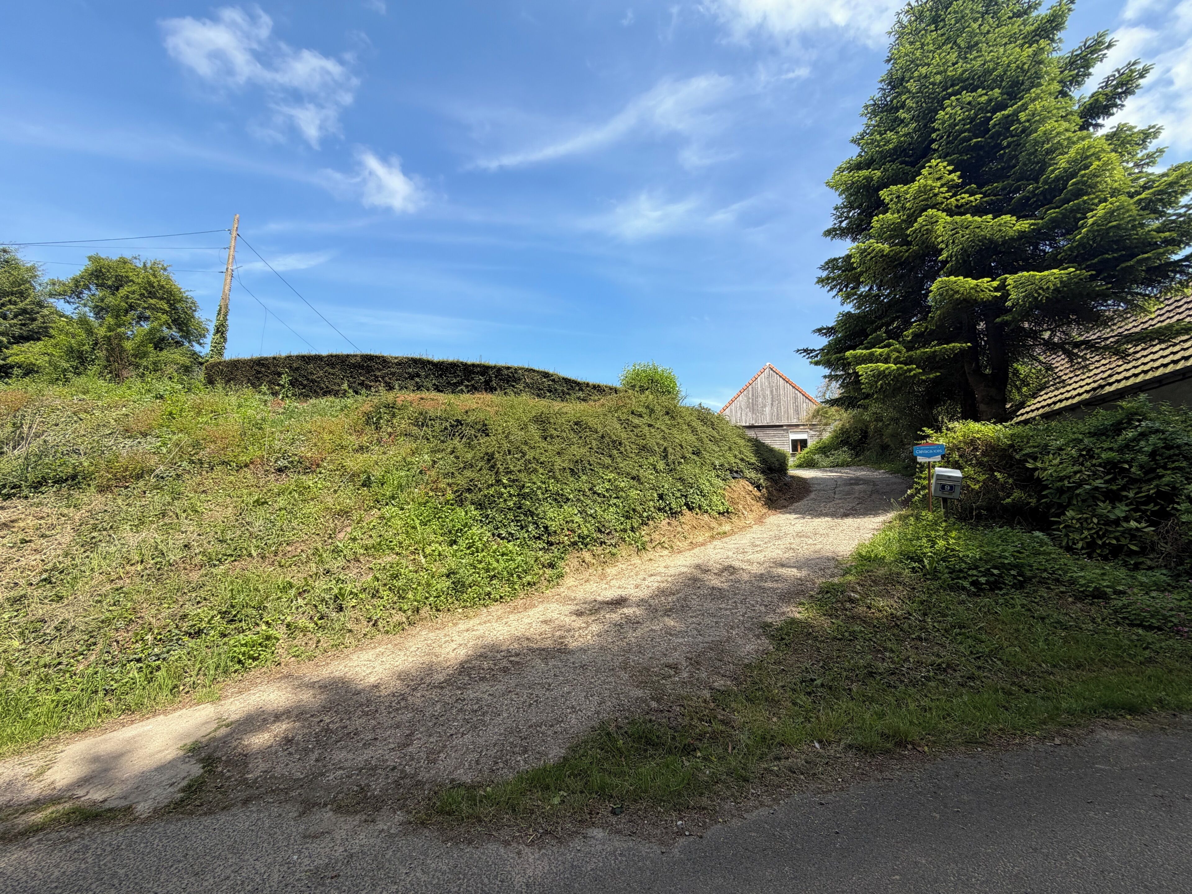 Una strada rurale che conduce a un edificio con tetto rosso, immerso nel verde sotto un cielo sereno.