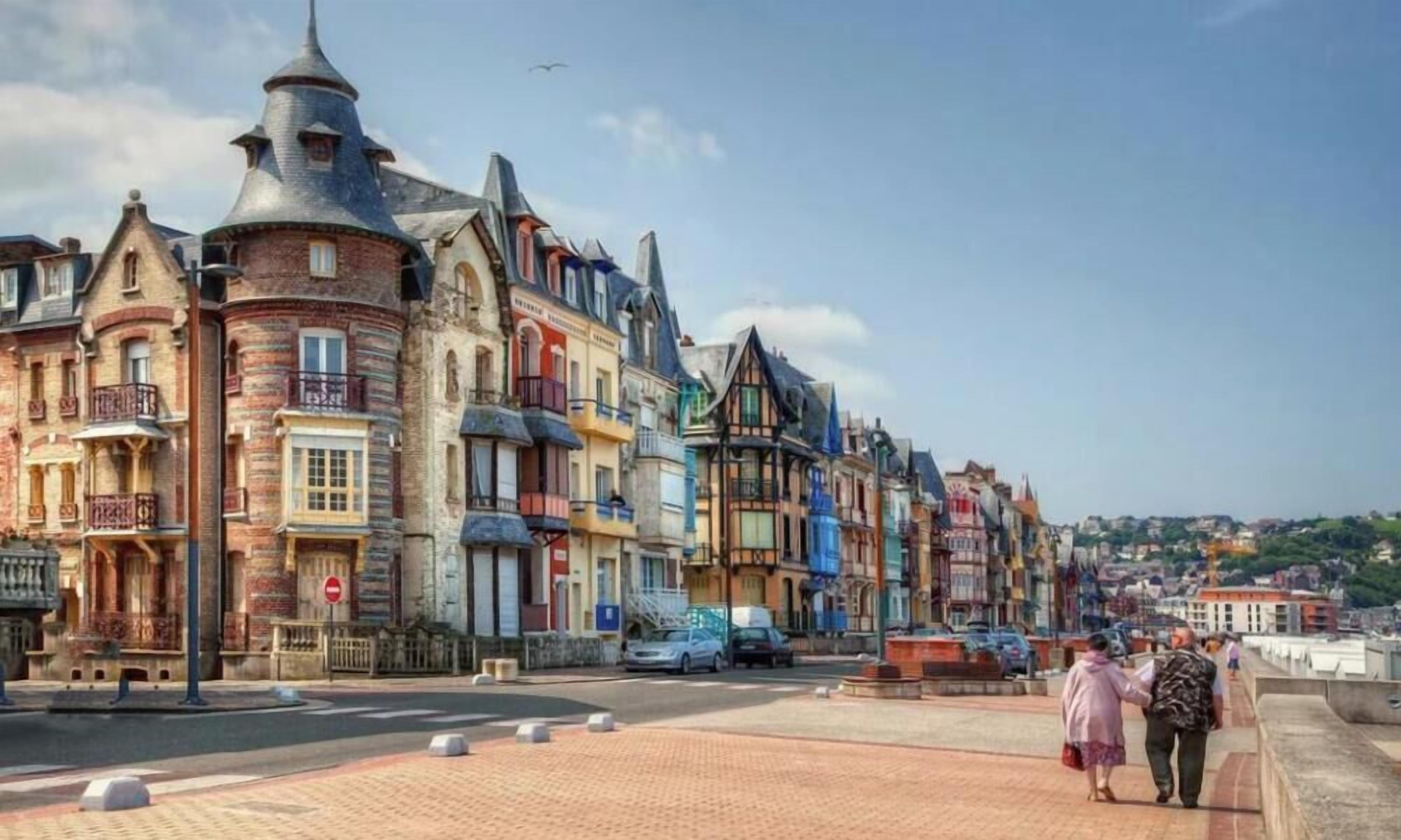 Eine Straße mit bunten Häusern, einem gepflasterten Gehweg und einigen Passanten.