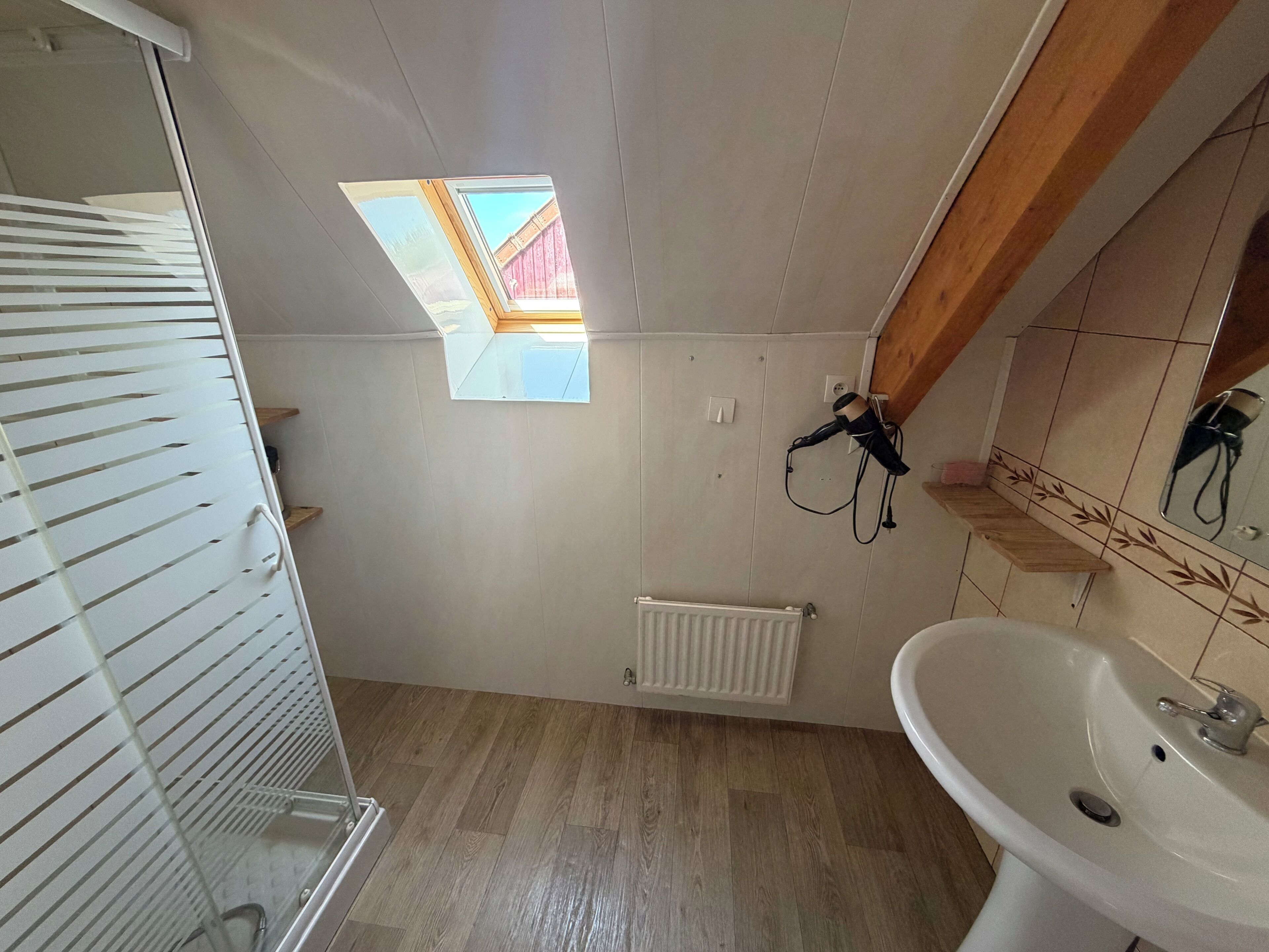 A bathroom with a skylight, a radiator, a sink, and a hairdryer.