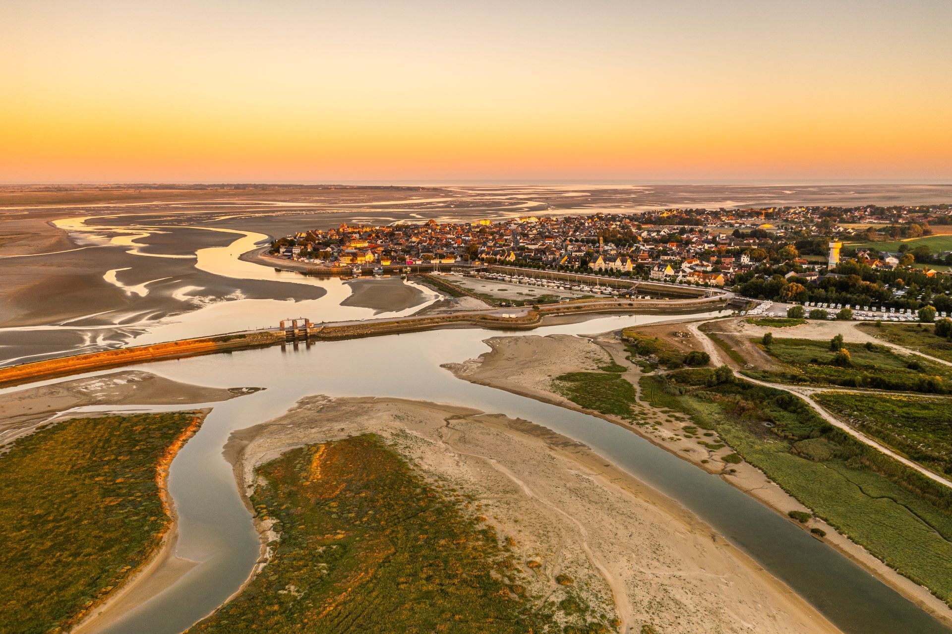 An aerial view of a coastal town with a river, a bridge, and a densely populated area with buildings.