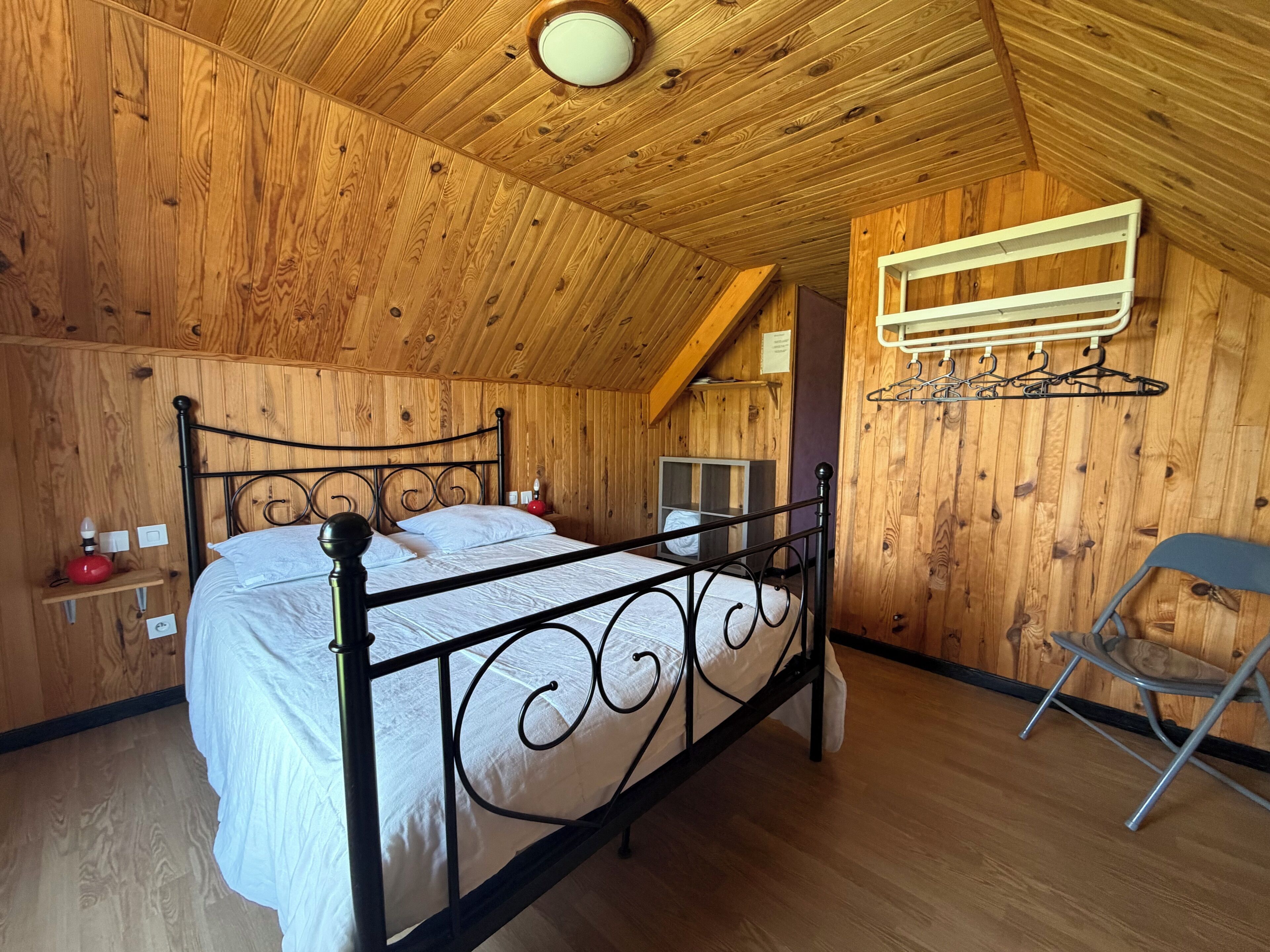 Habitació amb panells de fusta, un llit, una cadira i un estendal fixat a la paret.