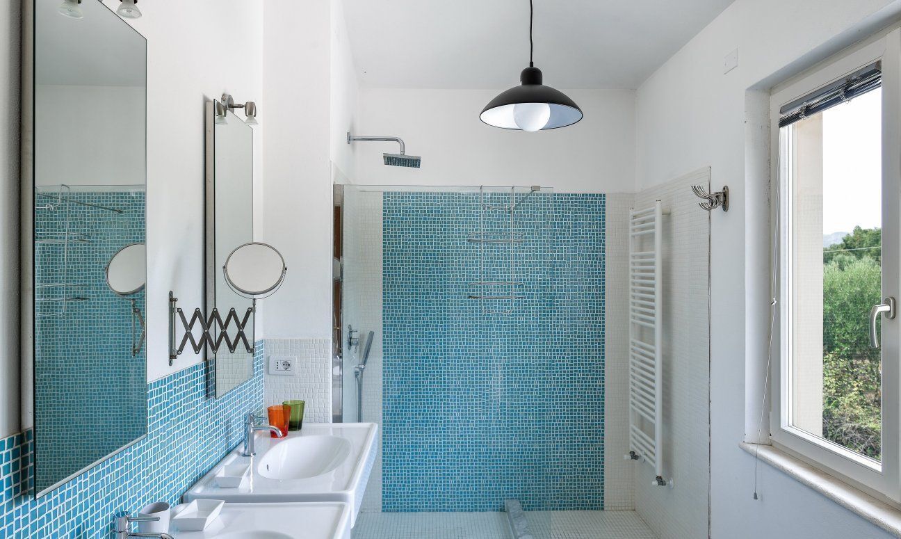 Un bagno con un lavandino bianco, uno specchio, una doccia e una finestra.