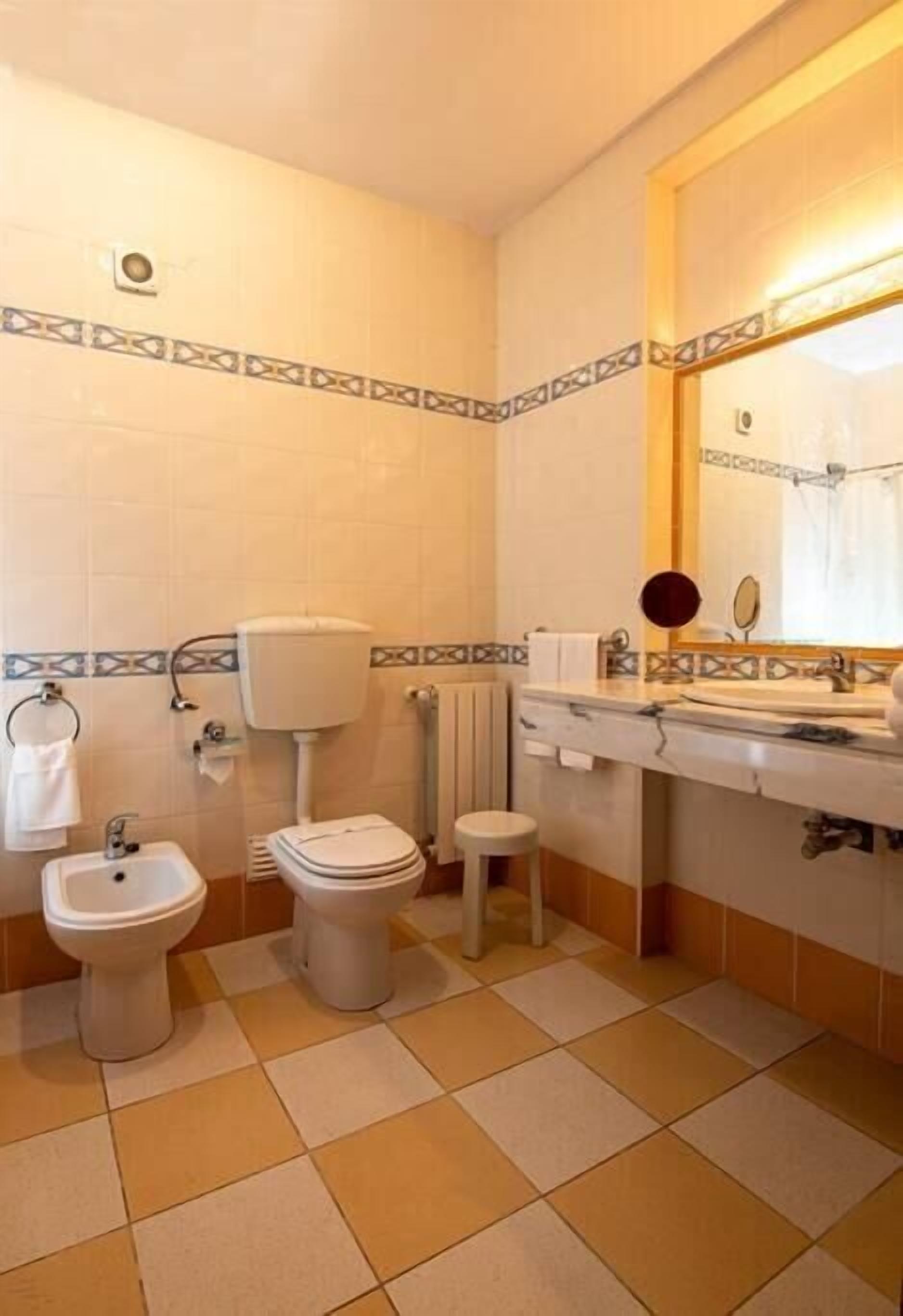 A bathroom with a toilet, bidet, sink, and mirror.