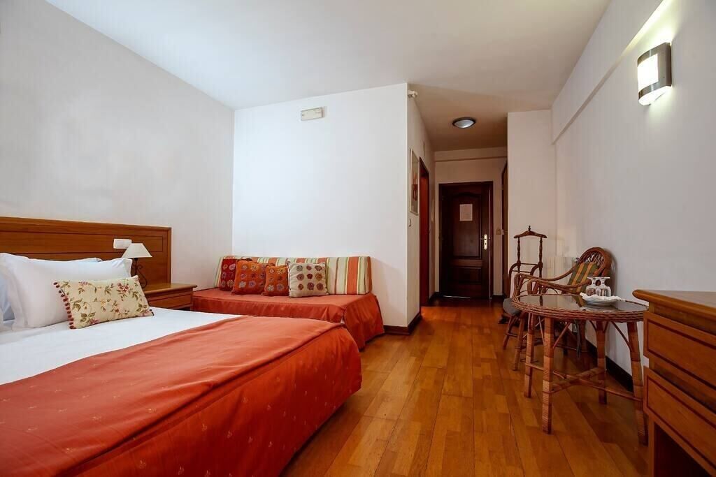 Une chambre d’hôtel avec deux lits, une tête de lit en bois, une petite table avec des chaises et un luminaire fixé au mur.