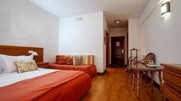 Une chambre d’hôtel avec deux lits, une tête de lit en bois, une petite table avec des chaises et un luminaire fixé au mur.