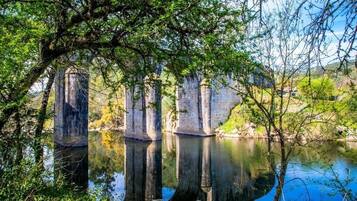 Een vredig uitzicht op de rivier, met stenen gebouwen weerspiegeld in het kalme water, omgeven door weelderige begroeiing.