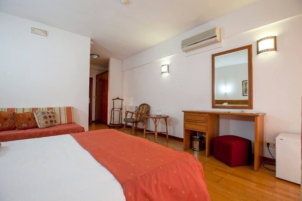 Een slaapkamer met een bed, een bureau, een stoel, een klein tafeltje en een spiegel.