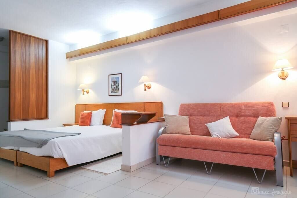 A modern bedroom with a wooden bed, a sofa, and two wall-mounted lamps.