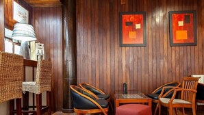 Un rincón acogedor con sillones de mimbre, un pouf rojo, mesas de madera y piso de baldosas.
