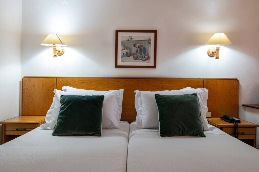 A double bed with two pillows, a wooden headboard, bedside tables with lamps, and a framed picture on the wall.