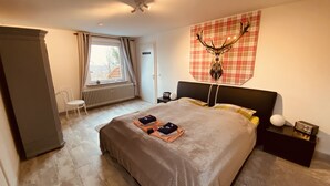 A bedroom with a large bed, a wall-mounted deer head decoration, a window with curtains, a radiator, and a small table with a radio. - Beautiful and spacious holiday home (Bad Harzburg)