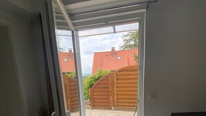 An open sliding glass door leading to a patio area with a view of neighboring houses and a wooden fence. - Beautiful and spacious holiday home (Bad Harzburg)