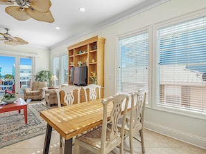 A spacious living room with a wooden dining table, comfortable chairs, a television, and a bookshelf.