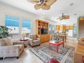 A spacious living room with patterned furniture, a television, and a kitchen in the background.
