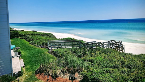 A beachfront property with a wooden deck, lush greenery, and a view of the ocean. - Seamist #6-Oceanfront-Wonderful View! (Seacrest)